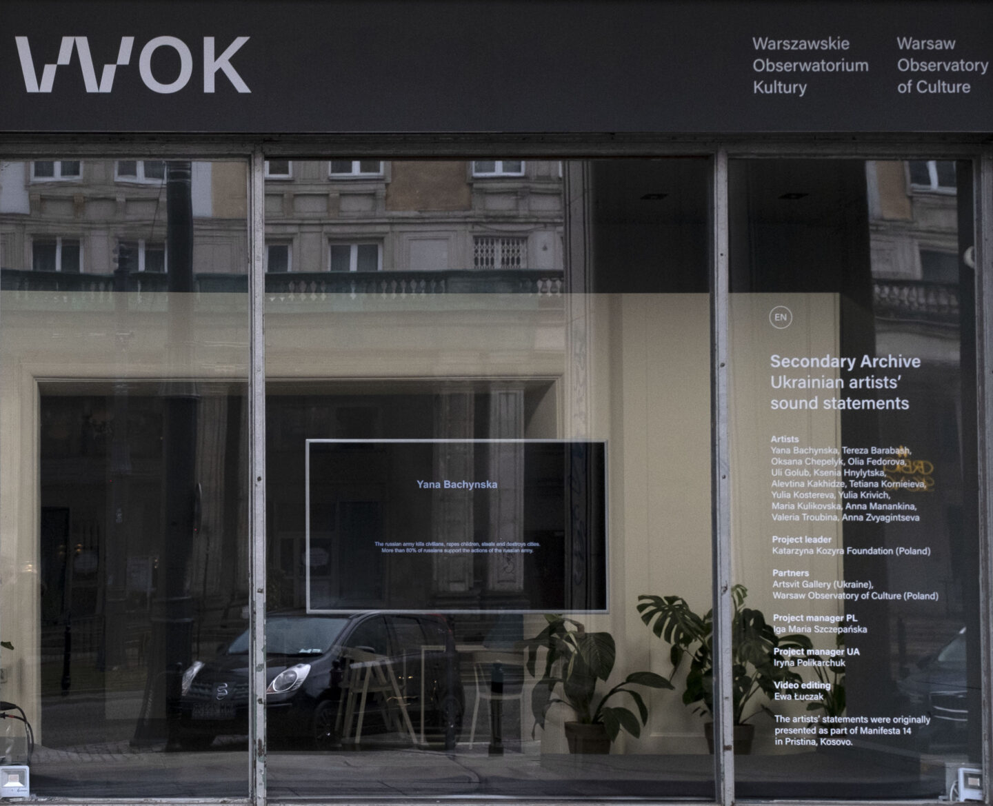 witryna WOK Lab widziana od strony ulicy Marszałkowskiej, w której widać telewizor z wystawą Secondary Archive Głosy ukraińskich artystek oraz jej opis na szybie