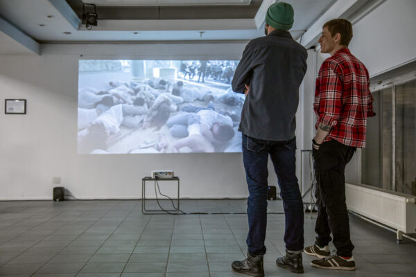two men looking at a projection showing refugees screened on a wall