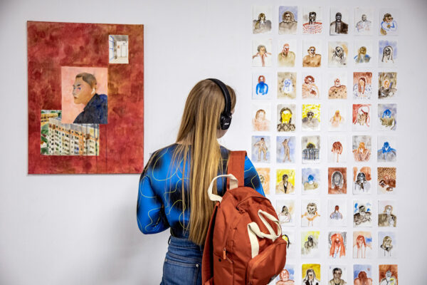 a woman in headphones looking at artworks at an exhibition of Belarussian residents