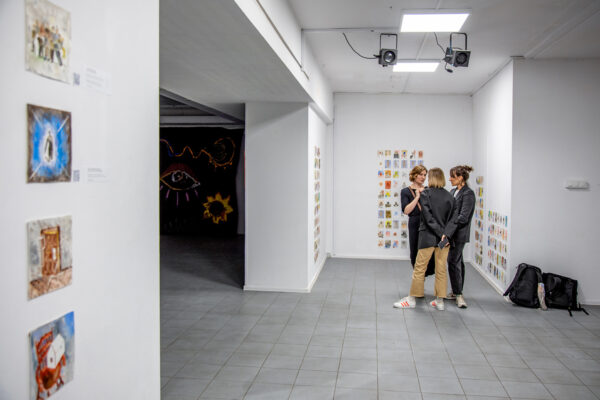trzy kobiety rozmawiają stojąc w przestrzeni WOK Lab, na ścianach wisi wystawa stworzona przez rezydentów białoruskich