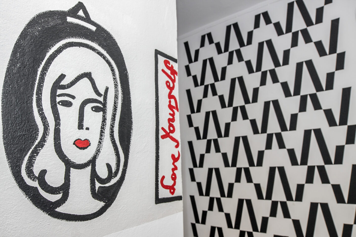 walls at the WOK office – on the left a portrait of a woman and a red sign saying “Love yourself”, in the background a repeat pattern made of black Ws