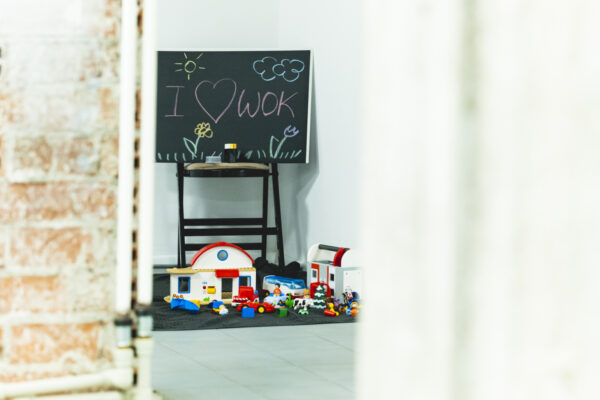part of a brick wall in the WOK Lab space, in the background a blackboard with chalk drawings in different colours and scattered children’s building blocks